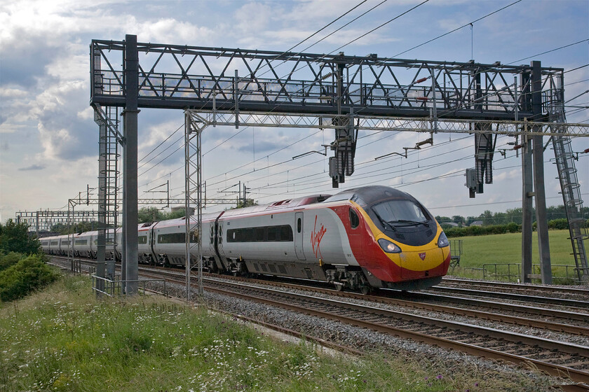 390127, VT 17.50 Birmingham New Street-London Euston (1B76), Roade Hill 
 An image very similar to the previous one. Another eleven car Pendolino passes Roade Hill. This time, 390127 is seen passing under the huge and ridiculously over-engineered signal gantry that carries just two colour lights working the 17.50 Birmingham to Euston Virgin service. 
 Keywords: 390127 17.50 Birmingham New Street-London Euston 1B76 Roade Hill Virgin Pendolino