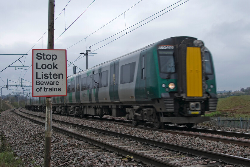 350407, 07.56 London Euston-Birmingham New Street (1Y17, 1L), Wilson's Crossing 
 I took a bit of a gamble by choosing to go to the well-known spot at Wilsons Crossing near Kingsthorpe in Northampton due to massive development in the area including Northamptons Northern Relief road crossing the line close by. Not knowing if the crossing was even open I trudged across the semi-flooded fields to find it in use but heavily fenced and signs asking walkers to wait before being given permission to cross certain spots due to construction traffic movements; it always used to be a peaceful and quiet spot to visit! 350407 passes the crossing working the 07.56 Euston to Birmingham New Street 1Y17 service. I deliberately chose a slow shutter speed to gain some motion blur to emphasise the safety notice at the foot crossing. 
 Keywords: 350407 07.56 London Euston-Birmingham New Street 1Y17 Wilson's CrossingLondon Northwestern Desiro