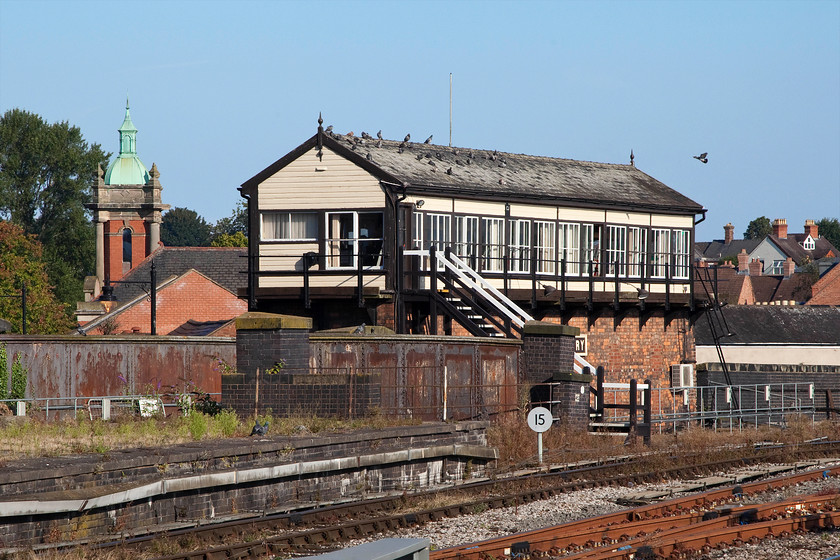 Shrewsbury Crewe Junction signal box (LNWR, 1903) 
 The pigeons appear to like the roof of Shrewsbury Crewe Junction signal box as they take in the early morning summer sunshine. The box is a charming LNWR structure built in 1903. Just in view is the end of its impressive wooden name board that acts more a running in board for passengers that simply says Shrewsbury. It looks as though the box is of a conventional construction. But, due to its elevated position from road level it towers above ground level striking quite sight when sitting in a car waiting at traffic lights on Cross Street. In the background is the striking Italianate tower of the former Shrewsbury congregational church. This has been used as commercial premises and, at the time of writing, is subject of a planning application for it be turned into apartments. 
 Keywords: Shrewsbury Crewe Junction signal box