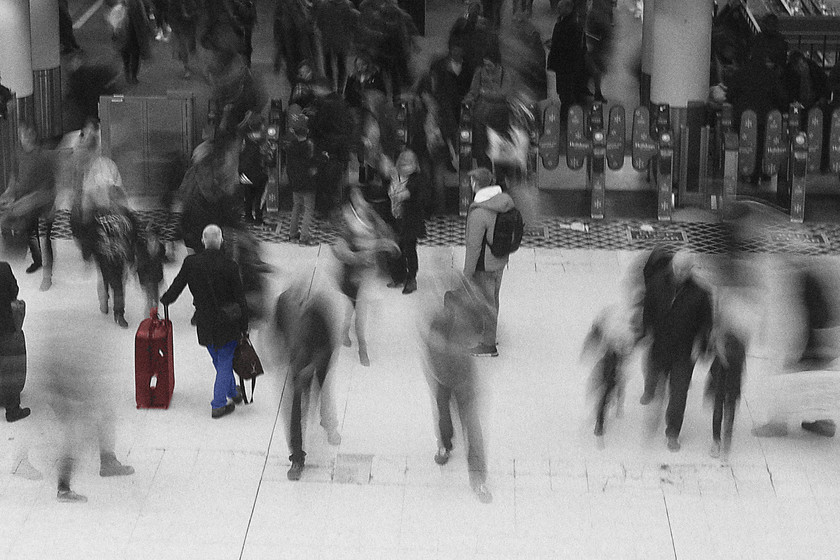 Concourse, London Waterloo station 
 Whilst standing on the mezzanine level high above the concourse at Waterloo I became conscious of the chap simp[ly leaning on his case awaiting his train to be called. As I was observing him, a pretty full train from Exeter St. David's arrived and disgorged its passengers. They all rush around this chap as they make their way busily on to wherever they happen to be going. In Photoshop I desaturated the image and played a little with the levels. I also allowed the original colour of the chap waiting to be re-introduced as a new layer. Finally, I introduced a little noise and grain that gives the image a more genuine kind on black and white 35mm feel.

Canon G1X Mk.III, 32.5mm, ISO 100, f.14, 0.6/sec