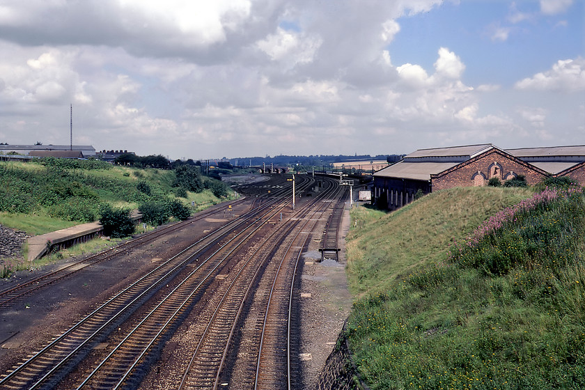 MML looking north with Wellingborough MPD from Mill Road 
 The view looking north from Wellingborough's Mill Lane bridge. It shows the up and down slow and fast lines with some sidings and, to the right, Wellingborough's former steam shed (15A, later to become 15B). At this time Wellingborough still stabled and fueled diesel (WO) but on the day of our visit only a lone and unidentified Class 25 could be seen. Today the shed still exists and is the process of being turned into a supermarket with this scene is very similar apart from the recent arrival of the electrification masts. However, taking this equivalent photograph needs a ladder as Network Rail has installed totally ridiculous concrete parapet extensions. 
 Keywords: MML looking north with Wellingborough MPD from Mill Road