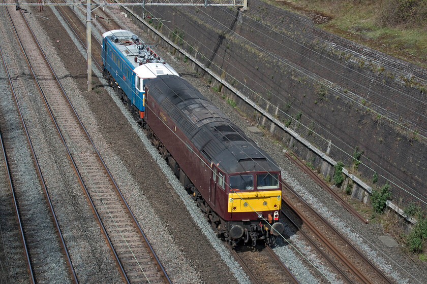 86259 & 47772, 12.04 Acton-Rugby CS (0X86, 3L), Roade cutting 
 After a day of railtour duties 86259 'Les Ross/Peter Pan' usually makes its way back to its weekday base in Rugby's rather overgrown carriage sidings. However, today it has company in the form of 47772 that was being towed dead and also ending up at Rugby. The duo, running as 0X86, is seen passing through Roade cutting on a pleasant spring afternoon. 
 Keywords: 86259 47772 12.04 Acton-Rugby CS 0X86 Roade cutting AC AL3 WCR West Coast RailwaysPeter Pan Les Ross