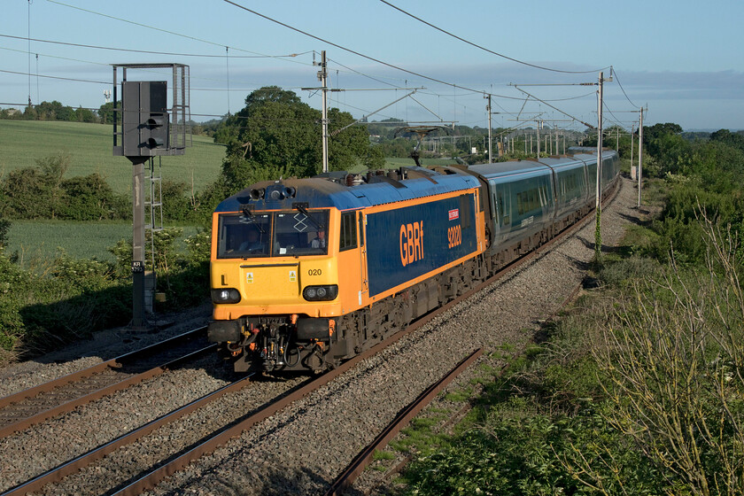 92020, CS 20.45 Inverness & 19.50 Fort William-London Euston (1M16, 2E), Milton crossing 
 92020 'Billy Stirling' runs bang on time past Milton crossing just north of Roade cutting on a bright spring morning. It is leading the up Highland Sleeper that is composed of three trains that join together at Edinburgh that start from Fort William, Inverness and Aberdeen. Evoking days of the secondman note that there are two members of staff in the cab of 92020, perhaps some staff training is taking place? 
 Keywords: 92020 20.45 Inverness & 19.50 Fort William-London Euston 1M16 Milton crossing Caledonian sleeper Billy Stirling