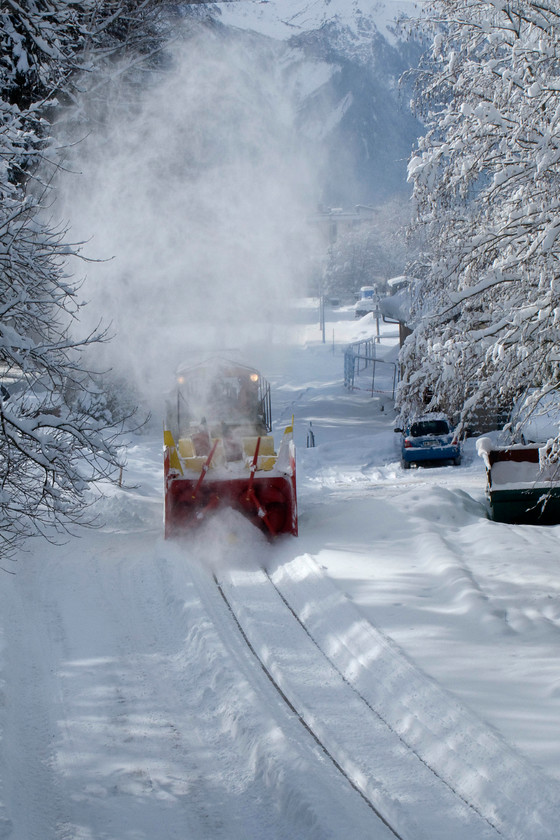 Snowblower, Chamonix Mt 
 Snow clearance in place French style! A diminutive one-metre gauge slow blower is prepared to go out on to the mainline in the Chamonix valley to undertake further clearance work. The picture is taken with some difficulty through the mesh of a footbridge that span the lines to the northern end of Chamonix statin. 
 Keywords: Snowblower Chamonix Mt. Blanc yard