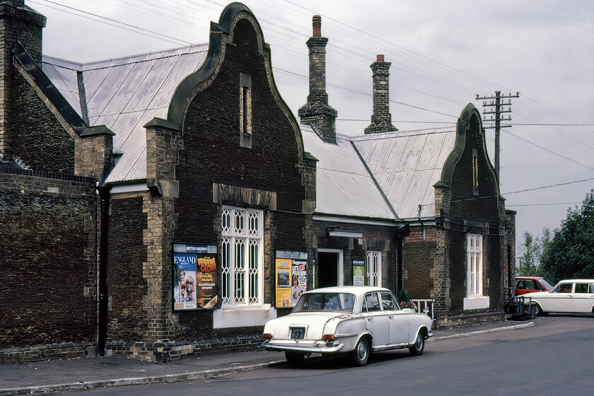 Frontage, Downham Market station 
 Back in 1981 I waxed lyrical in my notebook about Downham Market station building quoting from G. Biddles book Victorian Stations. He said of the station whos plain ogee gables and lozenge-latticed windows betokened a delightfully cosy simplicity entirely fitting in North Norfolk. Built in 1847 by the Lyn and Ely Railway it is constructed out of carrstone with pale brick dressings but I did note that the replacement white painted corrugated iron roof was not really in keeping! Thankfully, the roof has been returned to its original condition with the stone tiled roof now much more in keeping permitting the station to retain a Grade II listing by English Heritage. I am not sure that the tatty and rust-stained 1964 B registered Vauxhall Victor HB parked in front of the station will still be on the road! 
 Keywords: Frontage Downham Market station