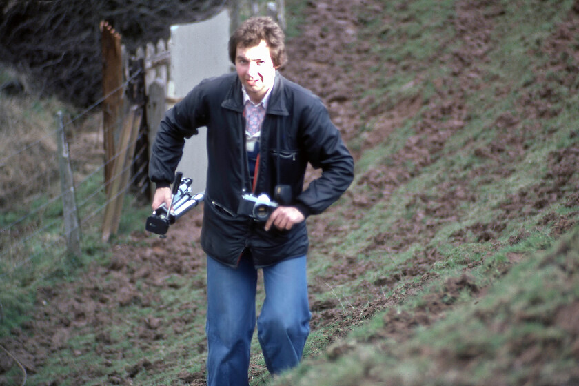 Dave Brush, negotiating the climb, Caerleon ST330923 
 With his tripod in one hand and holding his trusty Practika SLR in the other, my former teacher and railway enthusiast protg climbs a steep, grassy and muddy bank at Caerleon to a spot to capture the returning Welsh Marches Express charter. It was him along with Graham Vincent who encouraged a young schoolboy to get out on the lineside and take photographs and document all that was seen and I owe them a lot for that! 
 Keywords: Dave Brush negotiating the climb Caerleon ST330923