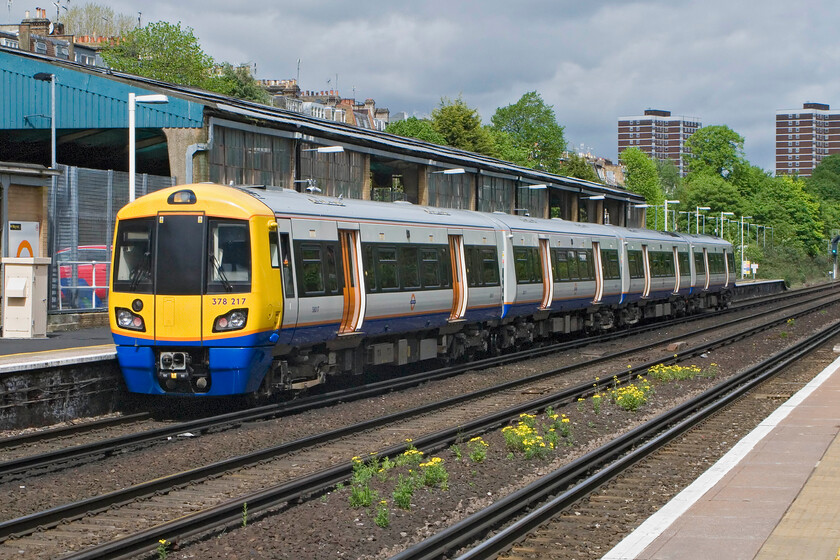 378217, LO 10.31 Clapham Junction-Willesden High Level, Kensington Olympia station 
 One of the recently extended (by one carriage) London Overground Capitalstars leaves Kensington Olympia station. 378217 is working the 10.31 Clapham Junction to Willesden High Level shuttle, terminating short due to engineering works. The large shed behind the train is the former Motorail terminal that is now in use as a car park. 
 Keywords: 378217 10.31 Clapham Junction-Willesden High Level Kensington Olympia station London Overground