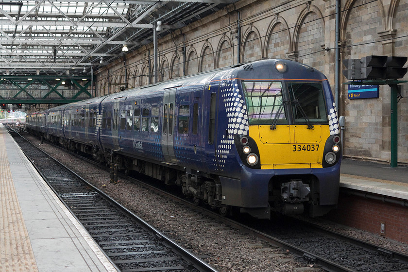 334037, SR 12.06 Edinburgh Waverley-Milngavie (2M19), Edinburgh Waverley station 
 ScotRail are the only operators of the forty three-car 334s that are part of the Juniper family. They were built in the early 2000s and have gone through two refurbishment programmes since then. At Waverley station, 334037 is leaving platform eleven with the 12.06 to Milngavie a journey that takes it through Bathgate and then through the middle of Glasgow via Central Low Level station before heading north out of the city to its destination. 
 Keywords: 334037 12.06 Edinburgh Waverley-Milngavie 2M19 Edinburgh Waverley station