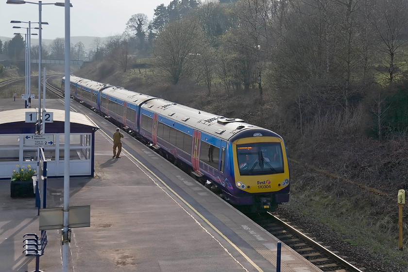 170304 & 170308, TP 16.55 Manchester Airport-Cleethorpes (1B86), Chinley station 
 I am not absolutely sure what Andy is doing in the strange pose on Chinley station as 170304 and 170308 passes forming the 16.55 Manchester Airport to Cleethorpes. Chinley station is a shadow of its former self with just one island platform and a large waiting shelter as seen just behind Andy. This is quite a contrast to when it had several platforms, four main running lines and extensive sidings including a turntable. There was a general post-war decline but the factor that completed the rot in the station's fortunes was the closure of the former Midland route from Derby through to Manchester in 1968. 
 Keywords: 170304 170308 16.55 Manchester Airport-Cleethorpes 1B86 Chinley station