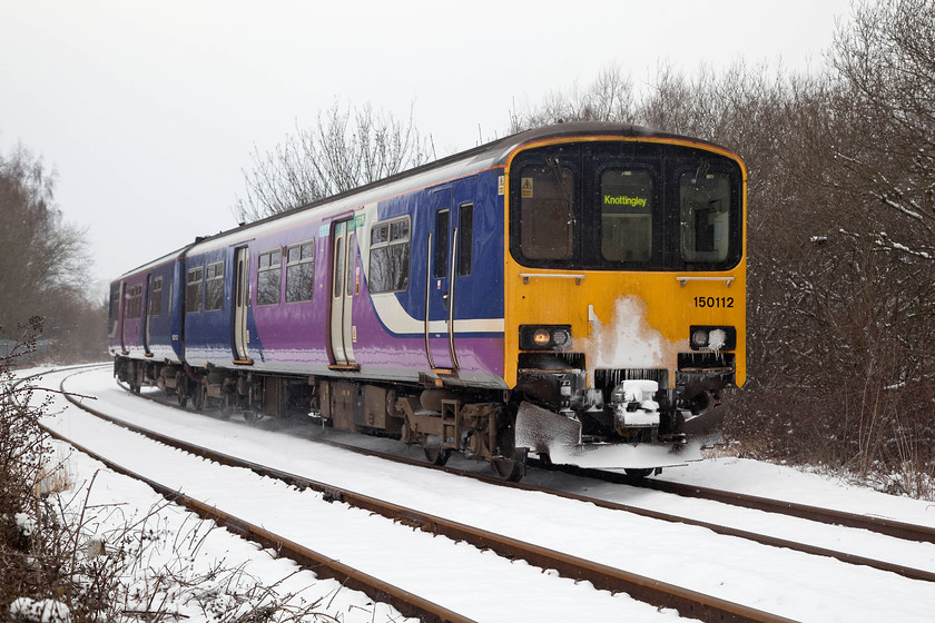 150112, NT 14.00 Leeds-Knottingley (2F19, RT), Cutsyke level crossing 
 A welcome break from the snow finds 150112 easing around the sharp curve at Cutsyke level crossing as it forms the 14.00 Leeds to Knottingley working. The line speed over the crossing is 25mph according to the most recent risk assessment data. There has been very little misuse of the crossing, probably down to the fact that rather than having raising and lowering barriers it has wheeled gates that I should imagine are more difficult to 'dodge'. 
 Keywords: 150112 2F19 Cutsyke level crossing