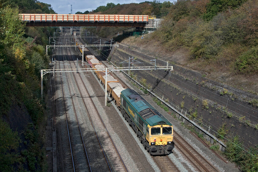 66588, 12.08 Denbigh Hall-Crewe Basford Hall (6Y70, 33L), Roade cutting 
 Switched off and going along for the ride 66588 is seen at the rear of the 6Y60 12.08 Denbigh Hall to Crewe Basford Hall engineering train. It appeared to be made up of a rake of loaded JNA Falcon wagons carrying ballast returning to Crewe for probable recycling. Leading the train, which is now largely out of sight under Roade's new bypass bridge spanning the cutting, is 66515. 
 Keywords: 66588 12.08 Denbigh Hall-Crewe Basford Hall 6Y70 Roade cutting Freightliner