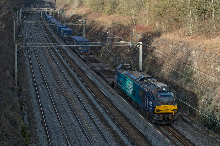 88010, 13.51 DIRFT-Tilbury (4L48, 2L), Hyde Road bridge 
 88010 'Aurora' leads the 13.51 DIRFT to Tilbury 4L48 up Tesco Express through the shadows of Roade cutting taken from the village's Hyde Road bridge. Again, a very lightly loaded train with possibly a dozen boxes with even more empty flats symptomatic of problems with the supply chain or of trade in general; can somebody enlighten me? Another week or so and the train would have been in full sunshine at this time of the day (14.15) in the depths of the cutting, bring on spring and the longer days! 
 Keywords: 88010 13.51 DIRFT-Tilbury 4L48 Hyde Road bridge DRS Direct Rail Services Aurora