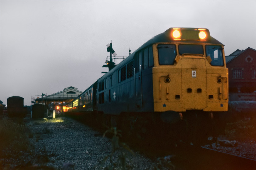 31132, 19.45 Weymouth-Bristol Temple Meads (2V72), Frome station 
 31132 is seen in virtual darkness at Frome station leading the 2V72 19.45 Weymouth to Bristol Temple Meads service. Past the light of the second Mk. I coach the station can be seen surrounded and supported by scaffolding in an effort to stop the structure from collapsing due to woodworm attack. Once again, I am not quite sure how Graham and I had the confidence to wander off the platform end, cross the single track and then stand in trackbed on the former down line to take this photograph.

There is an audio recording of this event on my youtube channel, see.... https://youtu.be/UF7jf-NFVMI 
 Keywords: 31132 19.45 Weymouth-Bristol Temple Meads 2V72 Frome station Brush Type 2