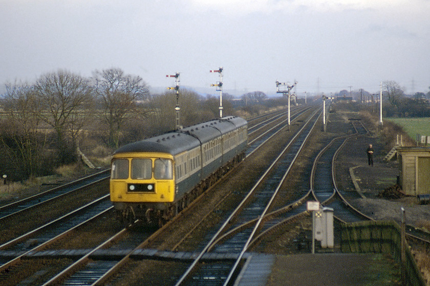 Class 124 DMU, 14.50 Hull-Leeds, Gilberdyke station 
 I really think that the Class 124 Swindon built DMUs were the most elegant built and despite being twenty years old when this photograph was taken look modern and purposeful. This unidentified set is seen passing Gilberdyke station with the 14.50 Hull to Leeds service with the passengers enjoying a good ride on this unit in relative luxury even if the fabled buffets had been removed by this time. Beyond the array of fine mechanical signalling is Oxmardyke signal box and notice the undulating track emphasised in this telephoto image. Graham can just be seen walking back towards the station having secured his photograph standing on the foot crossing the steps of which can be seen behind him. This foot crossing is still extant today but just traverses two tracks with the railway lined by tall trees; all so different than this wide open scene! 
 Keywords: Class 124 DMU 14.50 Hull-Leeds Gilberdyke station First generation DMU