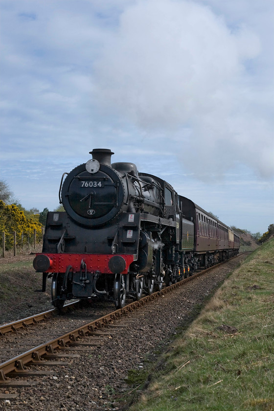 76034 (76084), 10.30 Sheringham-Holt, Wind Pump crossing 
 Having passed the 10.30 from Holt at Weybourne station 76084 (carrying the inauthentic 76034 number) brings the 10.30 from Weybourne past Wind Pump crossing on Kelling Heath. This is another example of a steam locomotive producing very little exhaust on this day with weather conditions conspiring against me coming up with a more dramatic photograph! Notice the recently cut embankments as this is a favourite area during the summer season for fires caused by hard-working locomotives producing many smuts and sparks. 
 Keywords: 76034 10.30 Sheringham-Holt Wind Pump crossing British Railways Standard Class 4MT 76084