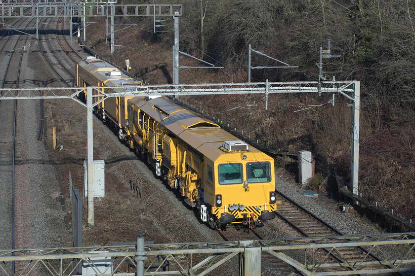 DR73117 & DR77907, 07.50 Watford London Concrete-Nuneaton Civil Engineers (6U48, 6L), A508 bridge 
 This is actually a 'going-away' view of the 07.50 Watford London Concrete to Nuneaton Civils move as it passes Roade. A forward shot would have been impossible from this location on the village's A508 road bridge as it would have been directly into the sun and it is far too dangerous to erect the requisite ladder on the south side with no pavement and much traffic! Network Rail owned Plasser and Theurer ballast tamper DR73117 leads (furthest away) with Ballast Regulator DR77907 nearest the camera. 
 Keywords: DR73117 DR77907 07.50 Watford London Concrete-Nuneaton Civil Engineers 6U48 A508 bridge Network Rail Plasser and Theurer 09-3X-D-RT diesel powered ballast tamper