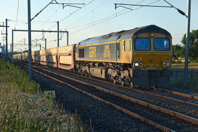 66745, 15.49 Garston Car Terminal-Dagenham Dock (6L48), Milton Malsor 
 66745 'Modern Railways The First 50 Years' leads the empty 15.49 Garston car terminal to Dagenham Dock car train. These wagons make a heck of a racket when they are not loaded with vehicles with a lot of noise from the resonating steel panels! The train is seen passing Milton Malsor that, as the milepost indicates, is sixty-two and a half miles from Euston. The sun is getting low in the evening sky now but does offer some lovely soft and warm light that makes a welcome change from the usual harsh and contrasty light of high summer days. 
 Keywords: 66745 15.49 Garston Car Terminal-Dagenham Dock 6L48 Milton Malsor