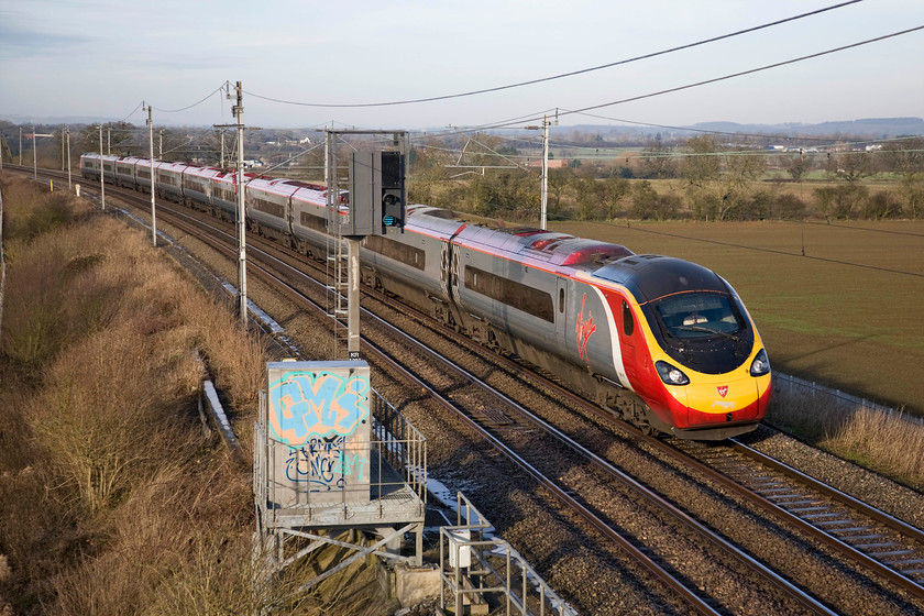 Class 390, VT 09.05 Wolverhampton-London Euston (1B04), Milton crossing 
 In glorious winter sunshine, an unidentified Class 390 Pendolino passes Milton Crossing working the 09.05 Wolverhampton to Euston service. This was a Sunday morning that had dawned cold and very frosty the remnants of which can be seen on the cable box covers next to the signal. 
 Keywords: Class 390 09.05 Wolverhampton-London Euston 1B04 Milton crossing Pendolino Virgin West Coast