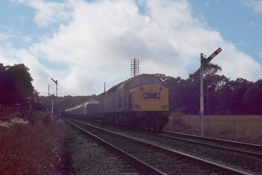 40199, up tanker train, Wennington SD621699 
 Technically this is not a great picture and was one that that was rescued from the original 1979 reject collection. Modern technology has resurrected it and a passable photograph is the result. 40199 gets away from Wennington behind 4472 'Flying Scotsman' that leading The North Yorkshireman railtour. I am not sure what train 40199 was heading but it seems to be composed mainly of some sort of tankers complete with barrier vehicles indicating it may be a particularly volatile load, can anybody advise? Notice that the semaphore arm has been removed from the lower post on the bracket signal. This arm once protected the junction just beyond the station where the now-closed Midland line diverged south westwards to join the WCML at Lancaster. 
 Keywords: 40199 up tanker train Wennington SD621699