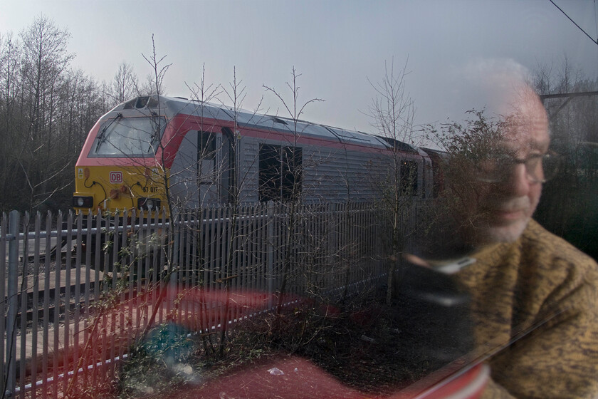 67017, stabled & Andy, Crewe LNWR 
 On the approach to Crewe from the direction of Stoke-on-Trent trains pass relatively slowly past LNWR's depot which often contains trainsets and locomotives from a variety of operators. With Andy's reflection making it appear that he is looking in the wrong direction one of Transport for Wales/Trafnidiaeth Cymru super train sets is seen stabled with 67017 on the end. Thier red and silver livery certainly strikes a pose looking a lot smarter than the previous operators' rather weak blue paint scheme. 
 Keywords: 67017 Andy Crewe LNWR Trafnidiaeth Cymru Transport for Wales