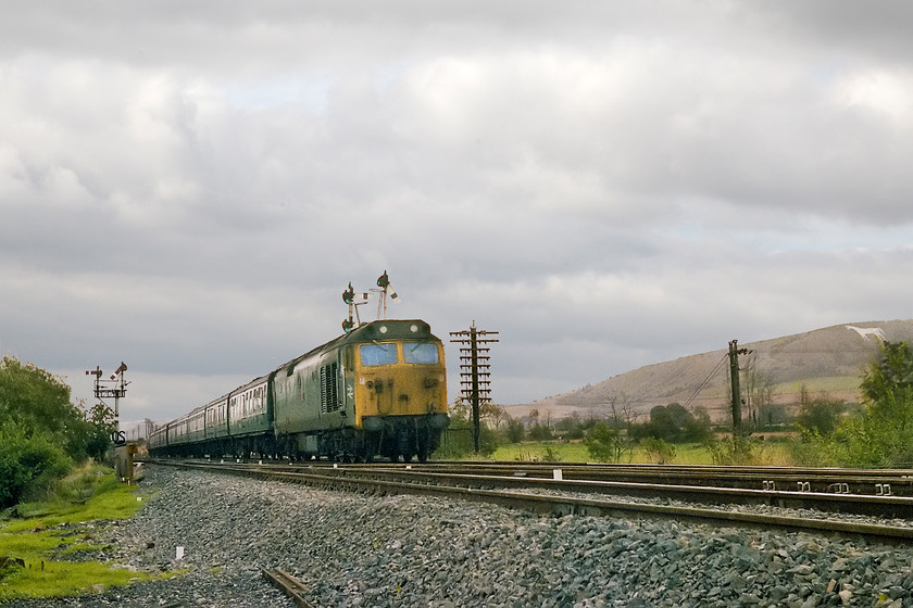 50044, 08.30 London Paddington-Paignton (1B34), Heywood Road Junction 
 The fact that 50044 'Exeter' has been taken slightly early and to one side enhances the interest contained in the image. It allows Westbury's iconic white horse to be seen clearly on the Salisbury Plain escarpment behind. It also allows the superb telegraph pole to be seen carrying the all important communication wires between the signal boxes. I am crouching in this spot at Heywood Road Junction with the permission with the signallman who had provided me with a hi-viz jacket for the occasion. As the two outer arms are lowered on the home bracket, the 08.30 Paddington to Paignton will not be stopping at Westbury but taking the avoiding line. I'll need to watch my back though as the up home is also pegged for a Paddington working. The left hand home arm at danger on the up bracket permits access to the now closed Westbury cement works sidings. 
 Keywords: 50044 08.30 London Paddington-Paignton 1B34 Heywood Road Junction