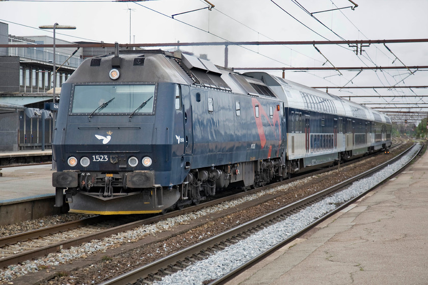 1523, 16.11 Copenhagen Central-Nykbing Falster, Roskilde station 
 With a lot of heat haze and exhaust Class ME 1523 gets away from Roskilde station leading the 16.11 Copenhagen Central to Nykbing Falster service. The ME was involved in a major accident at Haslev in April 1994 where it was hit by a double-headed freight hauled by MZ 1442 and 1439. Major damage was caused to all three locomotives that took two years to repair. 1523 also holds the accolade as being the first member of the class to emerge from the works in DSB's new blue livery in March 2002, the same design that it still wears today. 
 Keywords: 1523 16.11 Copenhagen Central-Nykbing Falster Roskilde station DSB Class ME