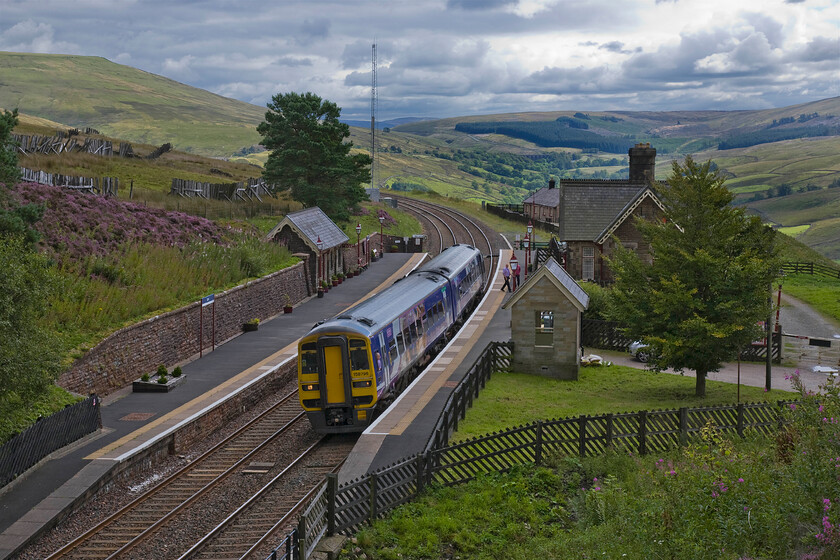 158796, NT 12.49 Leeds-Carlisle (2H88), Dent station 
 With the cloud having obscured the sun again it's a little gloomy up on the high fells at Dent station. Northern's 158796 pauses working the 2H88 12.49 Leeds to Carlisle service. The remoteness of Dent station is clear in this image as are the ramshackle remains of the snow fences off to the left. I must have stood in almost exactly the same position back in the summer of 1980 to take this photograph, see.... https://www.ontheupfast.com/p/21936chg/29532792004/x40047-down-freight-dent-station 
 Keywords: 158796 12.49 Leeds-Carlisle 2H88 Dent station Northern