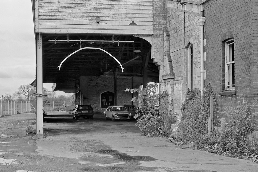 Loading gauge, former Trowbridge goods shed 
 The former goods shed at Trowbridge complete with its loading gauge still attached despite freight services being withdrawn and the tracks lifted in 1968. The shed was built in 1848 and was demolished in 1985 after becoming unsafe. At this time West Wiltshire District Council were attempting to list it just as celebrations were about to start commemorating the 150th anniversary of the Great Western Railway but BR had other ideas! Notice the cars parked inside, a close examination of the Austin 1100 reveals it was a particularly tatty example. The 'T' registered Mazda to the left was just over a year old at this time but it disappeared from the DVLA records in February 1983. 
 Keywords: Loading gauge former Trowbridge goods shed