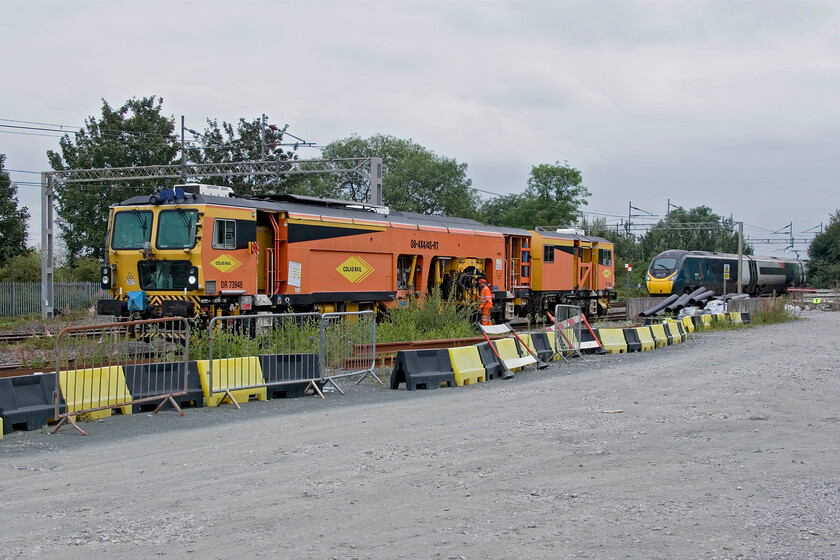 DR73948, stabled & 390148, VT 12.40 London Euston-Birmingham New Street (9G21, 10L), site of Blisworth station 
 The sidings that remain at Blisworth, where there was once quite a sizeable station, are often the home to some track machine or other. Today when passing there were also a number of vans and orange jackets about. As can be seen, Colas Rail Plasser and Theurer Switch and Crossing Tamper DR73948 is being worked on and ready for more work to come. To the rear, 390148 'Flying Scouseman' has just sounded its warning horn to the workers around and races past the scene working the 12.40 Euston to Birmingham New Street service. 
 Keywords: DR73948 390148 12.40 London Euston-Birmingham New Street 9G21 site of Blisworth station Avanti West Coast Pendolino Flying Scouseman