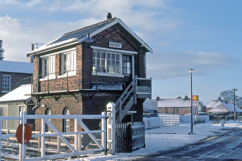 Haxby signal box (NER, c.1878) 
 Haxby signal box is seen in the crisp winter light with its wooden gates located on Station Road. The North Eastern Railway box is the earlier design of structure, the same type of which was seen yesterday at Oxmardyke, see.... https://www.ontheupfast.com/p/21936chg/29820607804/oxmardyke-signal-box-ner-north-eastern Note the garage selling both 3* and 4* petrol in the background. Based on the advertised price of 1.40 per gallon the current price for 4* would be 29p per litre. Incidentally, the garage still trading today but as a Jet franchise rather than Shell. 
 Keywords: Haxby signal box