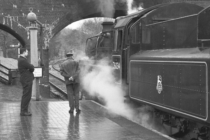 76034 (76084), 10.15 Sheringham-Holt, Weybourne station 
 With the light pretty flat at this end of Weybourne's station on the North Norfolk Railway I decided, when back on the computer, to have a bit of a play with this otherwise rather disappointing photograph. I cropped it down to try to build the human interest a little and have also desaturated it. To give it a more 'period' feel I then added a little grain. I also darkened down the platform to bring out the reflections and I actually quite like the result. The crew wait for the arrival of the returning service from Holt whilst 76034 (actually 76084) hisses to itself in anticipation of a departure leading the 10.15 Sheringham to Holt. 
 Keywords: 76034 76084 10.15 Sheringham-Holt Weybourne station NNR North Norfolk Railway Poppy Line British Railways Standard Class 4MT.