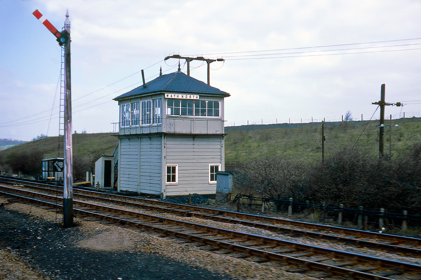 Wath North signal box (Midland, 1899) 
 Wath North signal box is passed at speed and looking at the box it appears empty suggesting that it may have been switched out. The box is classically Midland in its design dating from 1899 as is the superb Midland wooden signal post in the foreground complete with its finial. This box and the route between Wath Road and Goose Hill Junction soldiered on as a through passenger route for a few more years until mining subsidence made this impractical. The fast lines were removed first with the line continuing as a poorly used freight route until 1988. However, a spur was retained to serve the Ardagh glass factory at Monk Bretton that is still extant today (as of the time of writing in 2020) and receives regular sand trains from Middleton Towers in Norfolk. 
 Keywords: Wath North signal box Midland Railway