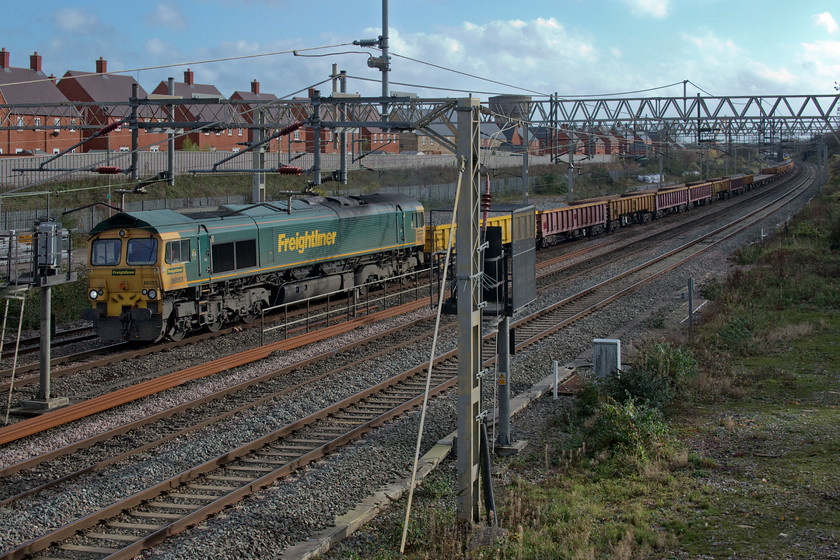 66553, 10.25 Hanslope Junction-Bescot up engineers (6Y62, 10E), site of Roade station 
 66553 leads a rake of loaded wagons containing tons of used ballast that is being taken for cleaning and recycling. The 6Y62 10.25 Hanslope Junction to Bescot is seen passing Roade. I took a bit of a gamble estimating that the Class 66 would fit between the signal and the stanchion and as can be seen here it does, by the skin of its teeth! Thanks to Mike for the reporting number. 
 Keywords: 66553 10.25 Hanslope Junction-Bescot up engineers site of Roade station