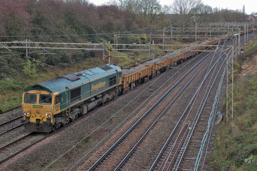 66553, engineering train after overnight possession at Blisworth, Ashton Road bridge 
 Leading a rake of JNA wagons loaded with used ballast eventually going for recycling at Bescot 66553 moves at walking pace along the up fast at Roade within sight of the previous train being led by 66587 'As One, We Can'. Whilst the first train left the section of possession at Hanslope Junction 66553 was to be held for some time by the mobile signalman just under Ashton Road bridge on which I am standing. 
 Keywords: 66553 engineering overnight possession at Blisworth Ashton Road bridge Freightliner