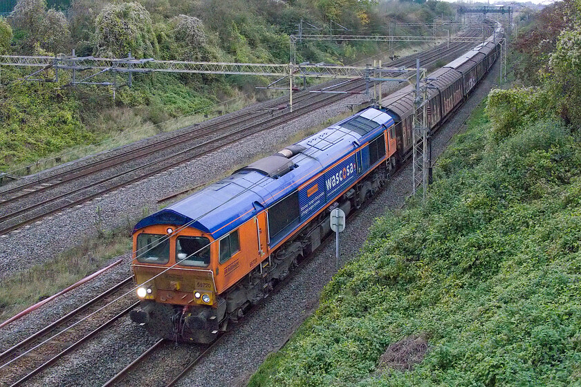 66720, 14.40 DIRFT-Dollands Moor (6O55, 8L), Victoria bridge 
 Leading the daily empty water train (6O55, 14.40 DIRFT-Dollands Moor), 66720 'Wascosa' passes Victoria bridge just south of Roade. The noise that the empty cargowagons make is instantly recognisable but the phenomenon when another train passes (as was about to happen here) is even more odd as the whole train seems to take on another resonance. 
 Keywords: 66720 14.40 DIRFT-Dollands Moor 6O55 Victoria bridge GBRf Wascosa