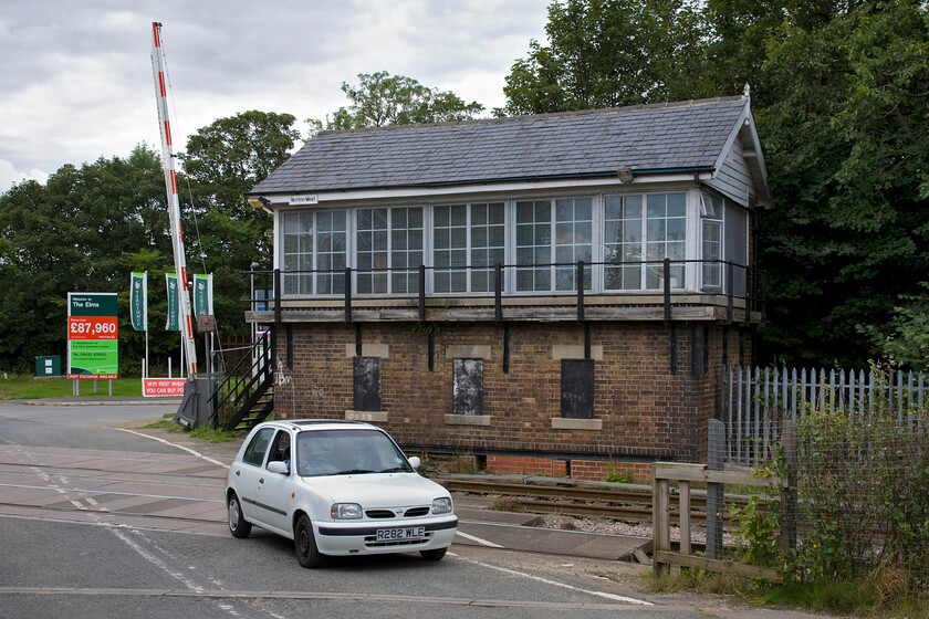 Norton West signal box (NE, 1910) & Andy driving R282 WLE 
 Norton West Junction signal box is a later and simpler North Eastern Railway design dating from 1910. It controls the semaphores at the western side of the triangular junction and the level crossing. The line coming from the northwest leaves the ECML just south of Ferryhill and usually carries only freight but also is a useful diversionary route. Indeed, two years ago (2012) it was a diverted Grand Central service that was involved in a SPAD incident here at Norton West whereby it crossed the level crossing in the foreground with the barriers raised having passed the protecting bracket signal NW36 whilst it was at danger. Andy is seen piloting his Nissan Micra across the level crossing towards me. 
 Keywords: Norton West signal box Andy driving R282 WLE North Eastern Railway Nissan Micra