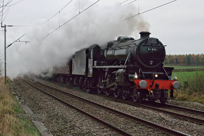 44871, outward leg of The Cheshireman, 07.10 London Euston-Chester (1Z63, 11L), Watford SP614688 
 Steam on the southern end of the WCML is becoming a bit of a rarity so I thoroughly expected The Chersirmean charter hauled by Black 5 44871 to draw the lineside crowds even on this very dull November morning! As such I decided to try out a spot that had been meaning to visit for some time, a small and isolated foot crossing across a couple of fields near the Northamptonshire village of Watford (of Watford Gap services fame). Just prior to the arrival of the charter I was joined by two others, Damien and Hayden from Wellingborough who had ridden on their bikes leaving at 05.00! I was a little undecided as to which side to take the photograph from opting for this view from the up side of the track thinking there was little wind to blow the smoke. In hindsight, I should have gone for the slightly more restricted down side as the smoke has drifted a lot more than I anticipated. Never mind, it was never going to be an award-winning image was it really! 
 Keywords: 44871 outward leg of The Cheshireman 07.10 London Euston-Chester 1Z63 Watford SP614688 Black five LMS Stanier Class 5 4-6-0