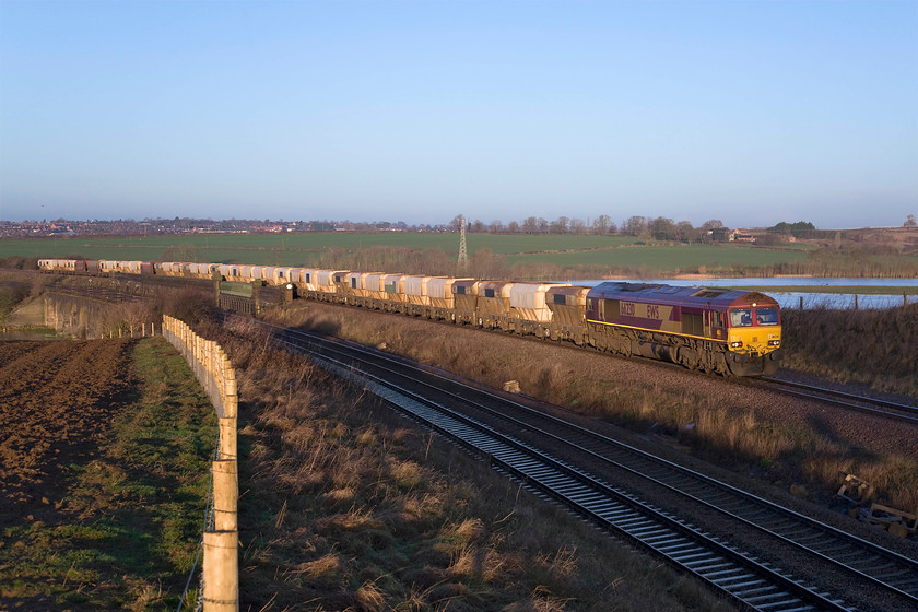 66230, 07.27 Mountsorrel-Radlett (6C31), Irchester Junction SP922673 
 66230 leads the 07.27 Mountsorrel to Radlett loaded stone train away from Wellingborough, seen in the background, on the now singled and bi-directional slow line. The wagons are still crossing the second viaduct that crosses the Nene Valley and river of the same name. The fast lines cross the other viaduct that is slightly lower named The Fourteen Arches so should the pair named The twenty-Eight Arches? Notice the recently installed fencing. I am surprised this type has been installed with Network Rail's crass obsession to install palisade fencing at every opportunity. Whilst this scene appears to be one of bucolic peace and quiet looks can be deceiving as a short distance behind me is the very busy A45 dual carriageway. 
 Keywords: 66230 07.27 Mountsorrel-Radlett 6C31 Irchester Junction SP922673