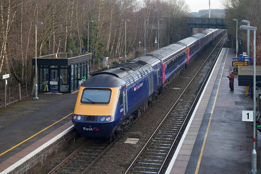 43004, GW 14.25 Great Malvern-London Paddington (1P57, 3E), Kingham station 
 The fortunes of Kingham station, opened in 1885, have waxed and waned over the years. It was once a very busy crossing point for a number of lines and boasted two signal boxes. As the inevitable closures took hold, rationalisation took place and, at one time, complete closure was a possibility. However, the line was spared and investment took place and Kingham's fortunes rose again. Passenger numbers are in the ascendancy, testament to this was the huge enlargement of the car parking facilities in 2015 to accommodate the commuter cars whose drivers want to use the station. Facilities remain a little basic but that can alway be improved on! Here, Andy watches 43004 at the back of the 14.25 Great malvern to London Paddington leave the station. 
 Keywords: 43004 1P57 Kingham station