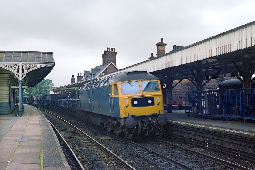 47337, up freight, Kettering station 
 47337 eases through the up slow platform at Kettering station with some wooden bodied 2-axle wagons and followed by a number of dogfish hoppers. On the right a parcels carriage can be seen sitting in the up facing bay platform surrounded by a number BRUTEs. This scene is still similar today apart from a massive new footbridge and the recent arrival of the electrification infrastructure that is extended, for the moment, as far as Corby. 
 Keywords: 47337 up freight Kettering station