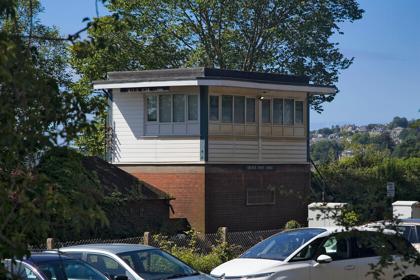 Grange-over-Sands signal box (BR, 1956) 
 During my last visit to Grange-over-Sands I photographed the BR (LM) box dating from 1956 from within the yard of the car repair business seen in the foreground, see... https://www.ontheupfast.com/p/21936chg/24425912004/grange-over-sands-signal-box However, perhaps as a sign of the times, the yard is now closed off with palisade fencing preventing access. Being a Saturday morning the gates were closed so a gap through the trees from the B5277 road has to suffice. 
 Keywords: Grange-over-Sands signal box BR 1956