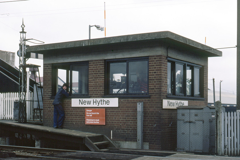 New Hythe signal box (SR, 1939)-31.12.80 
 New Hythe signal box would have won no prizes in the design awards! Built by the Southern Railway in 1939 to an austerity design it was a simple brick-built box with a single slab of concrete for the roof probably made at the company's Exeter plant where most of their railway infrastructure was manufactured. It controlled the level crossing into an industrial area on the Medway Estuary and was in use until 2005 when the crossing was replaced by a huge bridge. With the abolition of the box, the block section was then extended from Snodland to the north to Aylesford to the south. I am not at all sure why the signalman and his friend are looking at me laughing and waving? Perhaps it's the sight of a Venture Scout complete with a fully packed rucksack and walking gear taking a photograph of a signal box! This was my final photograph of 1980 taken on New Year's eve. 
 Keywords: New Hythe Signal Box