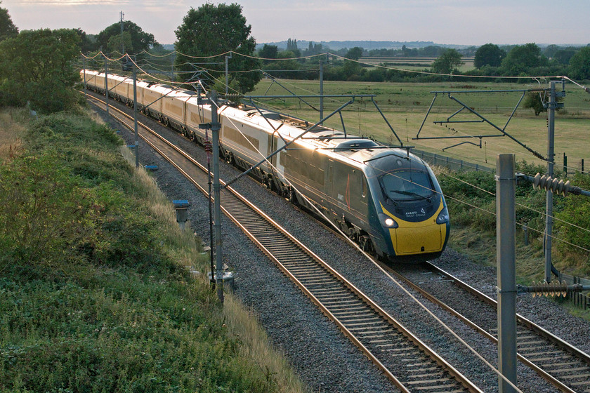 390103, VT 18.15 Manchester Piccadilly-London Euston (1A62, 20L), Wright's Lane bridge 
 Making good use of its tilting capabilities 390103 sweeps around a number of reverse curves on the Weedon loop avoiding Northampton. It is hurrying south working the 18.15 Manchester Piccadilly to Euston service and is seen about to pass under Wright's Lane bridge near the village of Gayton. I am not a fan of 'glint shots' finding them to be a little hackneyed but I do quite like this one it has to be said! 
 Keywords: 390103 18.15 Manchester Piccadilly-London Euston 1A62, 20L Wright's Lane bridge Avanti West Coast Pendolino