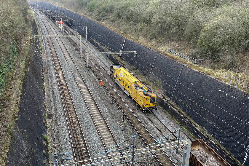 Trackwork, Roade cutting 
 A RAUK-2 Railvac machine makes easy work of removing the old ballast from the up slow line at the northern end of Roade cutting. The ballast is held in the centre section of the Sweedish built machine and then transferred to the wagons just seen to the lower right of the photograph. Whilst it was relatively early on a Sunday morning the noise emanating from deep in the cutting was pretty loud so it was good that this part of the line was remote and away from any housing! 
 Keywords: Trackwork, Roade cutting Railvac