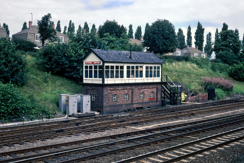 Kettering Junction signal box (LMS, 1935) 
 The LMS built Kettering Junction signal box in 1935 to replace two Midland boxes, one here and another slightly further south named Pytchley. This functional rather than attractive LMS designed box differs from the Midland boxes that it repaced by having a gabled roof and an attractive panelled brick base. This one controlled the double junctions of the crossovers between the fast and slow lines and the divergence of the single line to Huntingdon linking with the ECML. Notice the small extension to the steps at the far end of the box used by the signalmen for the exchange of the tokens for the said line. I have also seen a photograph taken inside the box of the unusual signal wire tightening device to take account of expansion during hot weather that would give inaccurate arm indication. 
 Keywords: Kettering Junction signal box