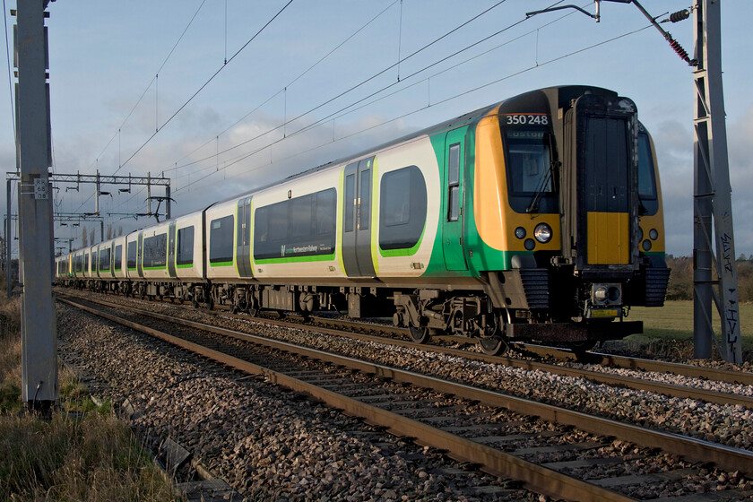 350248, LN 13.33 Birmingham New Street-London Euston (1W16, 10L), Wilson's Crossing 
 This is a real treat, taking a photograph of a train in full sunshine, something that I have not managed since the beginning of the month, see..... https://www.ontheupfast.com/p/21936chg/30022243387/x350369-10-37-northampton-birmingham! 350248 leads another Desiro past Wilson's Crossing to the north of Northampton with the 13.33 Birmingham New Street to Euston service. Normally on New Year's Eve, I would be commenting on the trains being full of revellers heading to the capital to join the celebrations but not this year (the same as last year too) with COVID stymying the usual activities. 
 Keywords: 350248 13.33 Birmingham New Street-London Euston 1W16 Wilson's Crossing London Northwester Desiro