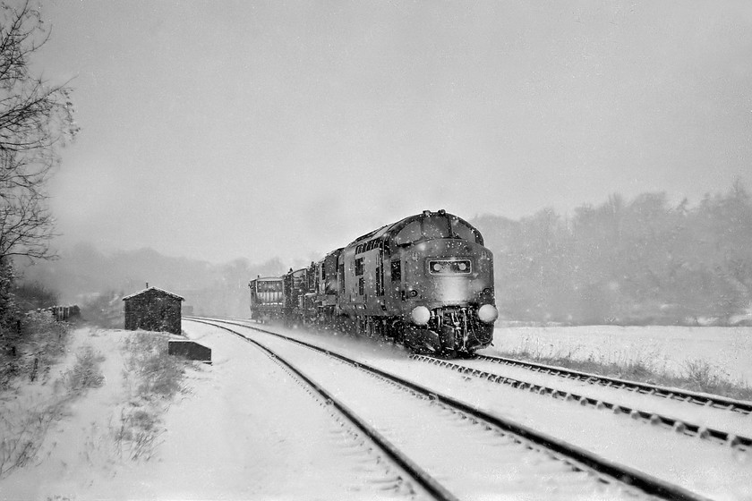 Class 37, unidentified engineering working, Avon Valley 
 In blizzard conditions, a class 37 makes its way along the Avon Valley between Freshford and Avoncliff. It is hauling a short train that includes, what appears to be a crane. Looking at the track in the foreground reveals them to be covered in snow indicating that there had been no trains along this line, it could have been a Sunday morning? 
 Keywords: Class 37 unidentified engineers` working Avon Valley