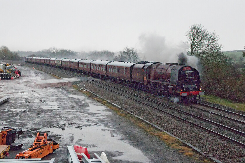 6233, outward leg of The York Yuletide Express, 06.12 Ealing Broadway-York (1Z25, 8L), Braybrooke SP769849 
 In the bitter wind, with the snow now falling again and with the train running late Andy and I were beginning to get very cold standing on a remote and exposed bridge near the village of Braybrooke at the northern extremity of Northamptonshire. The result of our exploits was this very poor photograph of former LMS Princess Coronation 6223 'Duchess of Sutherland' leading the outward leg of The York Yuletide Express running as 1Z25. Unfortunately, for the passengers who had paid a premium price to travel behind a steam locomotive, their enjoyment was to be terminated a short distance further north at Leicester where 6233 was removed with 47802 brought from the rear to haul the train forward. This left the Duchess to run light engine to Barrow Hill where it was watered, serviced and turned on the triangle rather than the turntable (it was just too big for that). The reason for its removal was not a failure but that the Leicestershire fire service tender that was to replenish its water supply at Humberstone Road was badly delayed. However, passengers aboard only arrived a few minutes adrift at York enabling them to explore the lovely city for a few hours before returning with 6223 once again leading. 
 Keywords: 6233 The York Yuletide Express 06.12 Ealing Broadway-York 1Z25 Braybrooke SP769849 Duchess of Sutherland LMS Princess Coronation Class