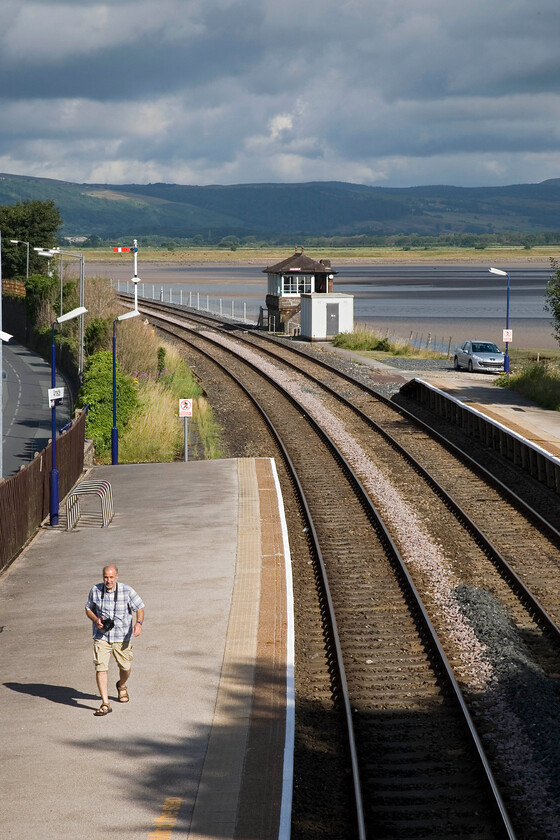 Andy, Arnside station 
 With the sun out and the Lake District in the background, it would have been great to stay on Arnside station a little longer but Andy and I were on a mission to get the boxes and station missed yesterday afternoon. Andy walks purposely along the platform and back to the car. After a short discussion, we decided not to head west towards Grange-over-Sands given the time it would take to drive all the way around the Kent Estuarry and then to return again so we decided to commence our journey south towards home. The missed stations and boxes would have to wait for another time.

NB We did eventually return in 2018, see.... https://www.ontheupfast.com/p/21936chg/C299765204/x3-to-stranraer-lakes-26-07-18 
 Keywords: Andy Arnside station