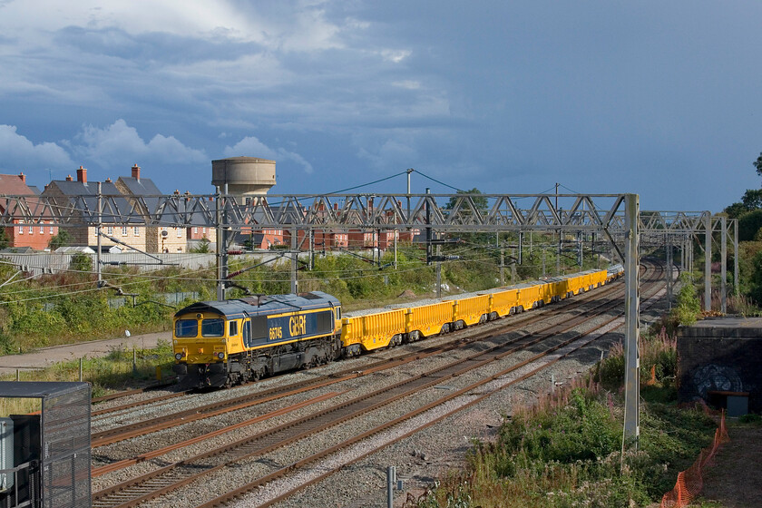 66745, 14.07 Bescot Yard-Wolverton (via Wembley) (6G57, 48L), site of Roade station 
 With the converted 'slinger' wagons resplendent in their bright yellow paint contrasting with a menacing sky the 14.07 Bescot Yard to Wolverton (via a seemingly pointless run to Wembley and back) passes Roade. 66745 is dead on the rear of the train but will lead the infrastructure working north once it reaches London. 
 Keywords: 66745 14.07 Bescot Yard-Wolverton via Wembley 6G57 site of Roade station GBRf